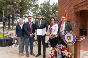5 people standing by American flag and EAC podium, 1 of which is holding an award.